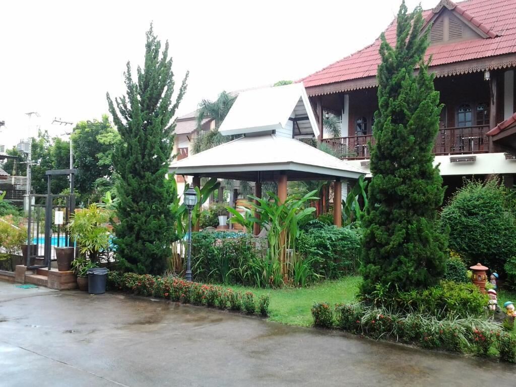 A traditional house with a red roof, surrounded by lush greenery and a covered patio area.