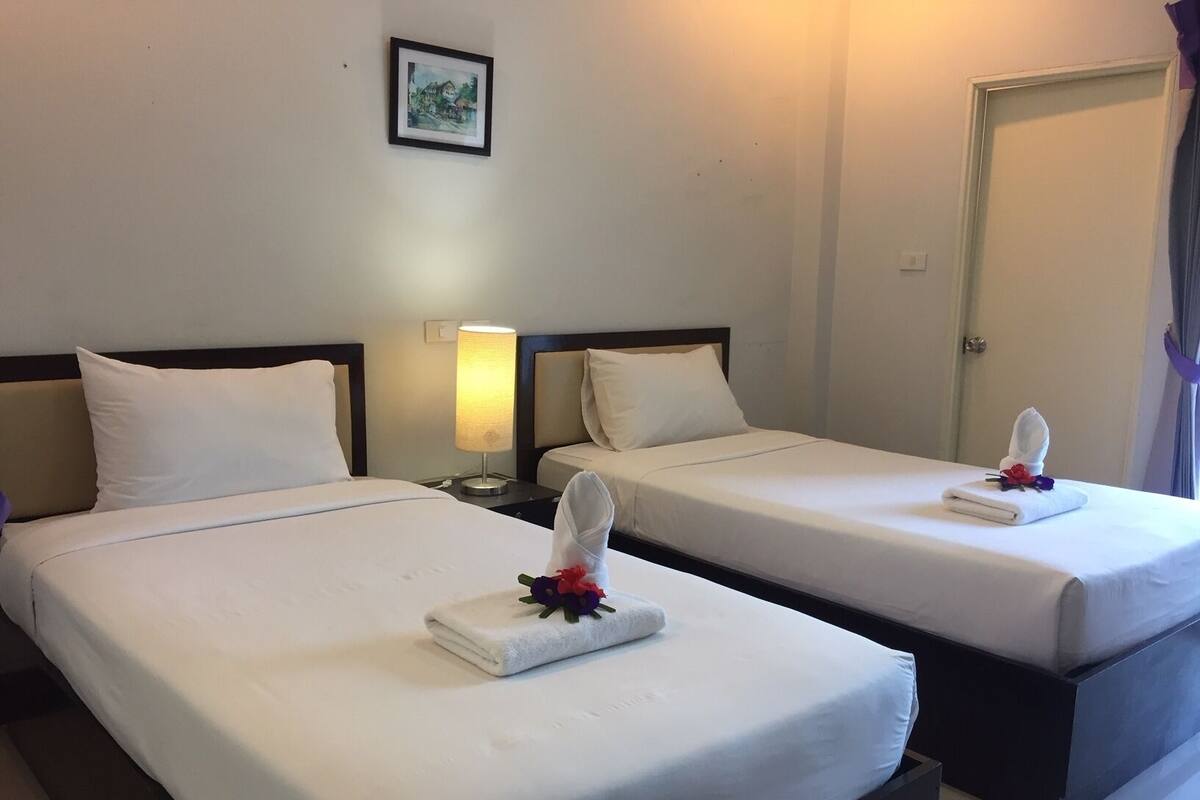 Two single beds with white linens, a bedside lamp, and a framed picture on the wall.