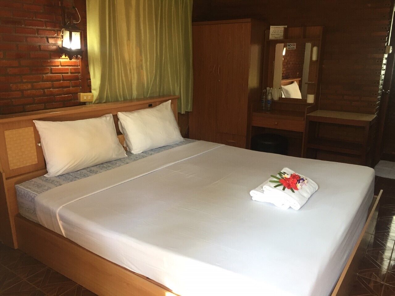 A neatly made bed with white linens, a wooden headboard, and a green curtain.
