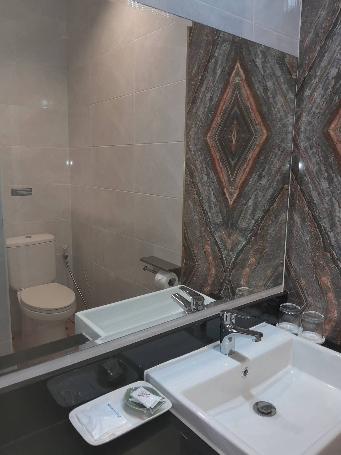 A bathroom with a white sink, a mirror, and a toilet. The wall has a patterned tile design.