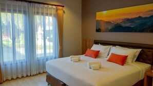 Une chambre d’hôtel avec un grand lit, du linge de lit blanc et des oreillers orange. Un tableau représentant un coucher de soleil est accroché au mur.