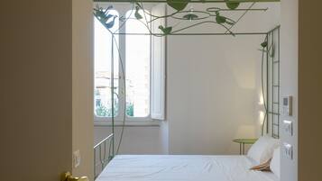 A bedroom with a bed, a window, a green plant, and a door.