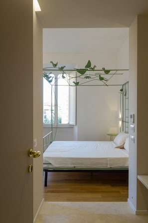 Un dormitorio con cama, ventana, planta verde y puerta.
