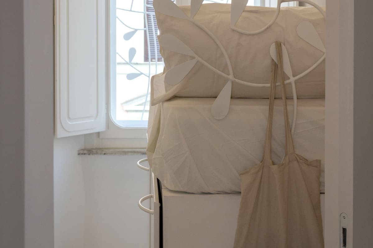A room with a window, a bed, and a hanging bag.