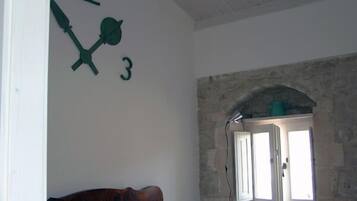 A room with a stone wall, a window with shutters, and a wooden headboard.