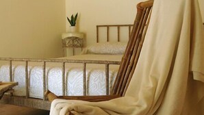 Een kamer met een bed, een stoel met een plaid, een klein tafeltje met een plant en een kamer met een patroon vloer.