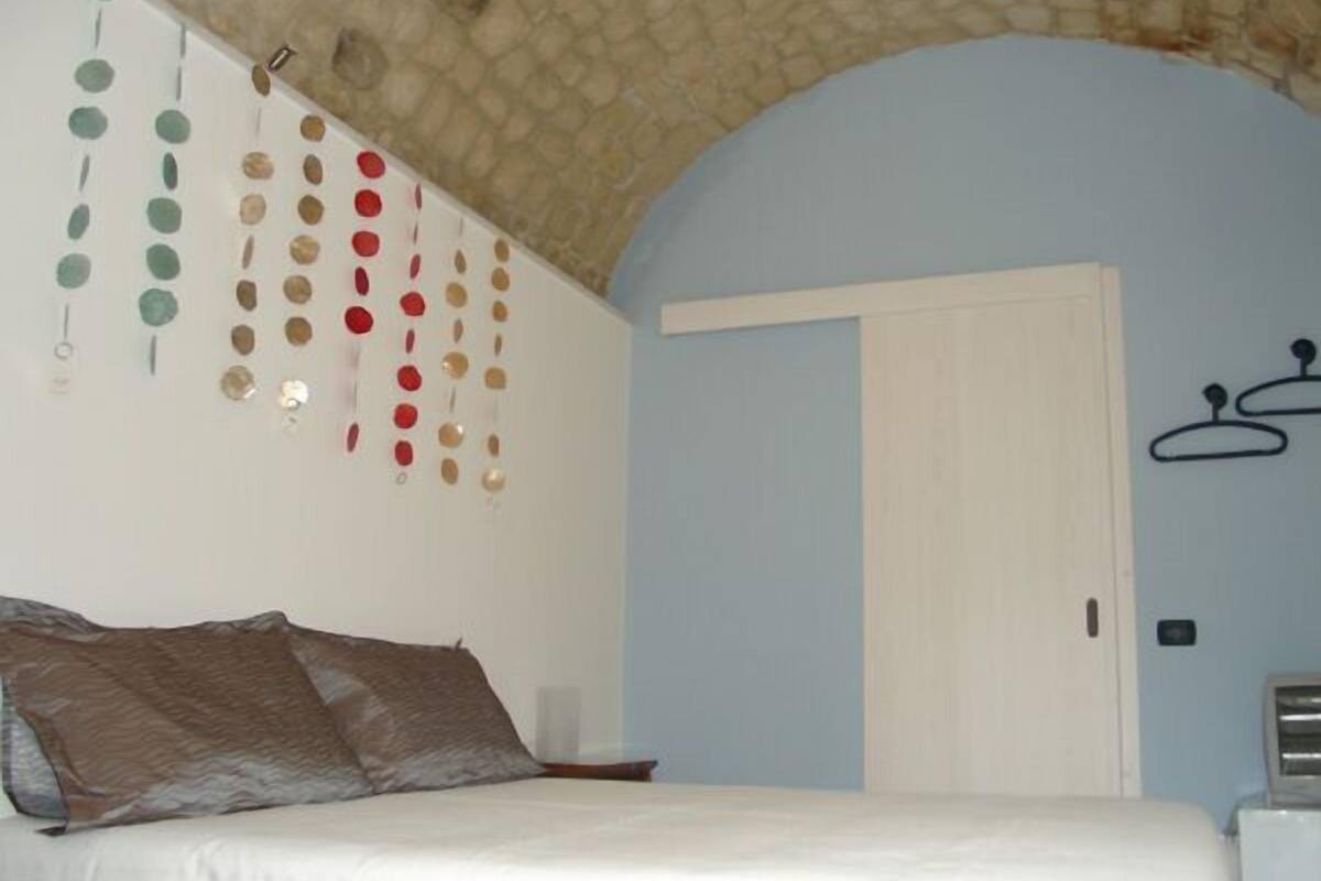 Une chambre à coucher avec un lit, un élément décoratif suspendu, une porte et un porte-manteau fixé au mur.