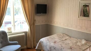 A room with a bed, a chair, a television on the wall, a radiator, and a window with curtains.