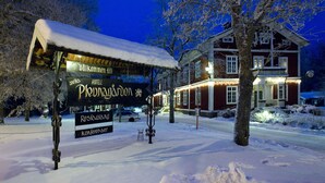 A snow-covered outdoor seating area with a sign for a restaurant and a building with illuminated windows in the background. - Hotell Plevnagården (Malmkoping)