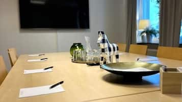 Une salle de conférence avec une longue table, des chaises, un téléviseur à écran plat et une fenêtre avec des rideaux.