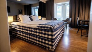 A hotel room with a large bed, a desk, a chair, and a view of the outdoors. - Hotell Gillet i Köping (Köping)