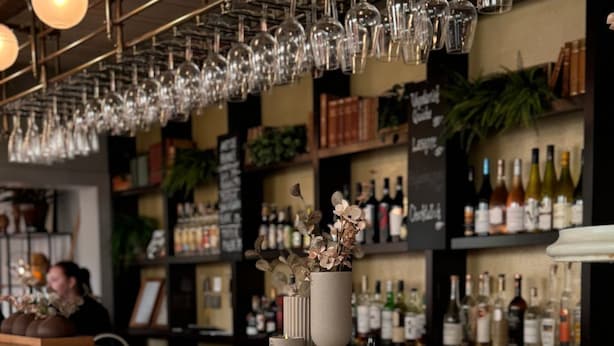 A bar area with a counter, hanging wine glasses, and shelves with bottles. - Hotell Gillet i Köping (Köping)