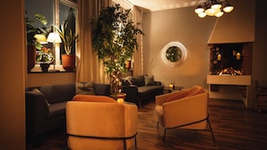 A cozy living room with a sofa, two armchairs, a large potted plant, a side table with a candle, and a fireplace. - Hotell Gillet i Köping (Köping)