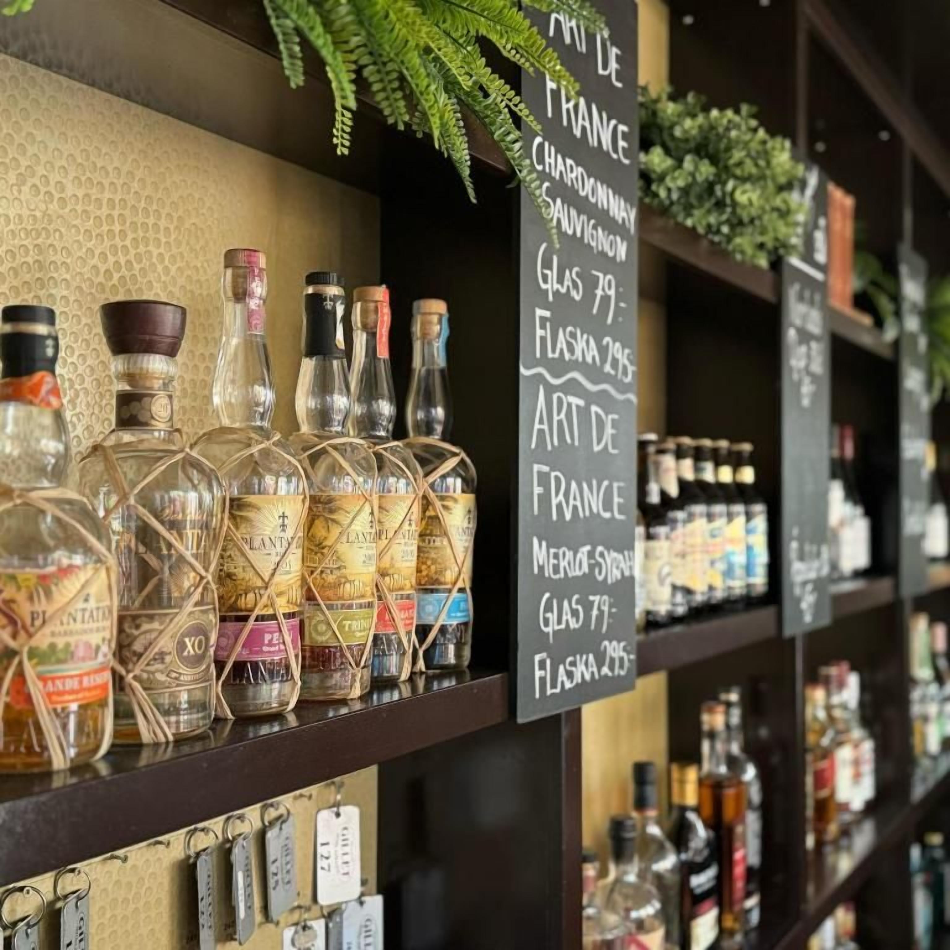 Zona de bar con estantes llenos de botellas de licor y una pizarra que muestra un menú con diferentes vinos y licores.
