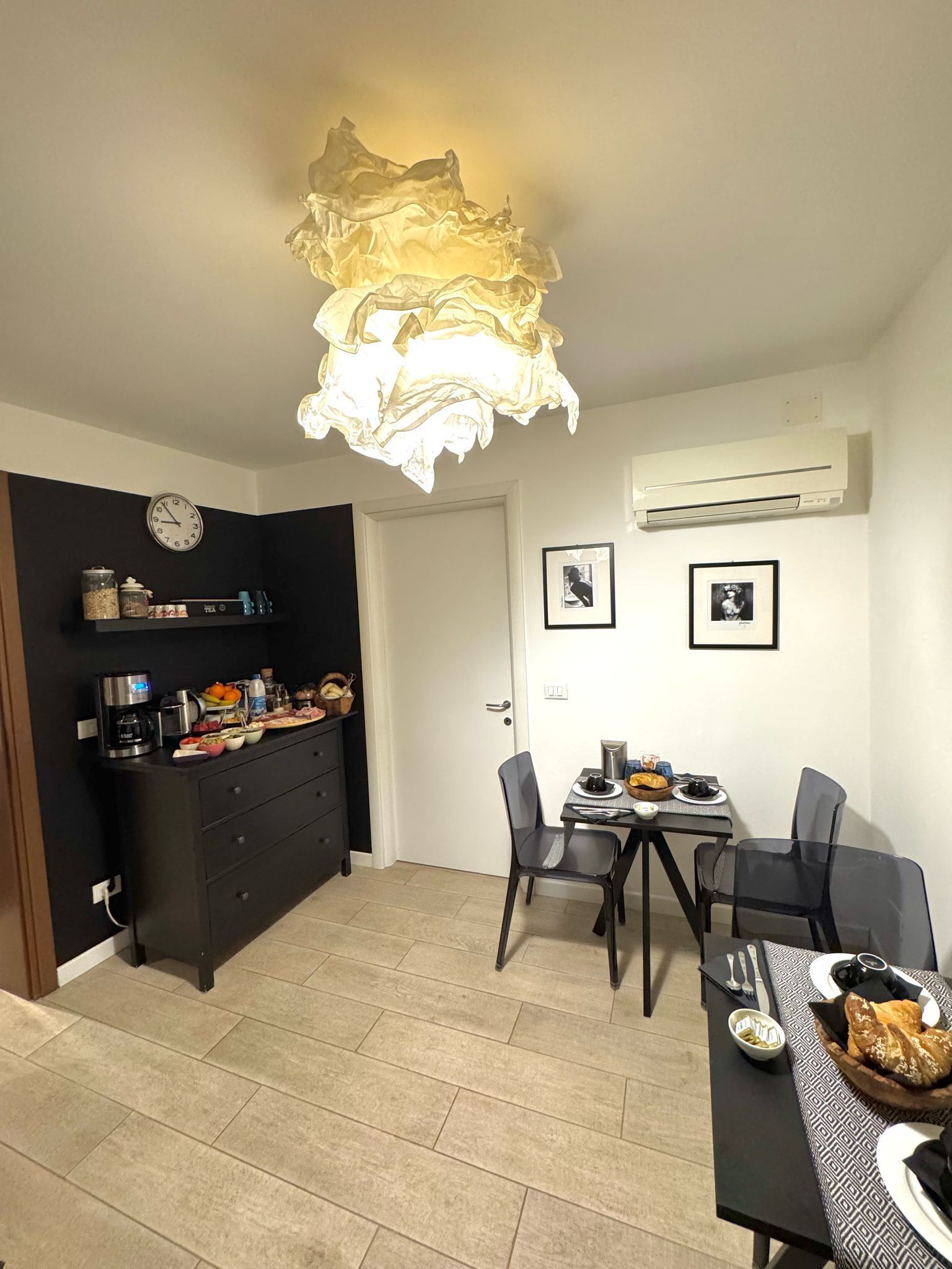 Una cucina compatta con zona pranzo, caratterizzata da un lampadario moderno, una sveglia e un condizionatore d'aria.
