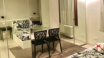 A modern bedroom with a large mirror, a bed with a floral bedspread, a small desk with a chair, and a radiator.