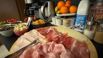 A wooden cutting board with various meats and a knife, a coffee maker, a fruit bowl, and a milk carton on a kitchen counter.