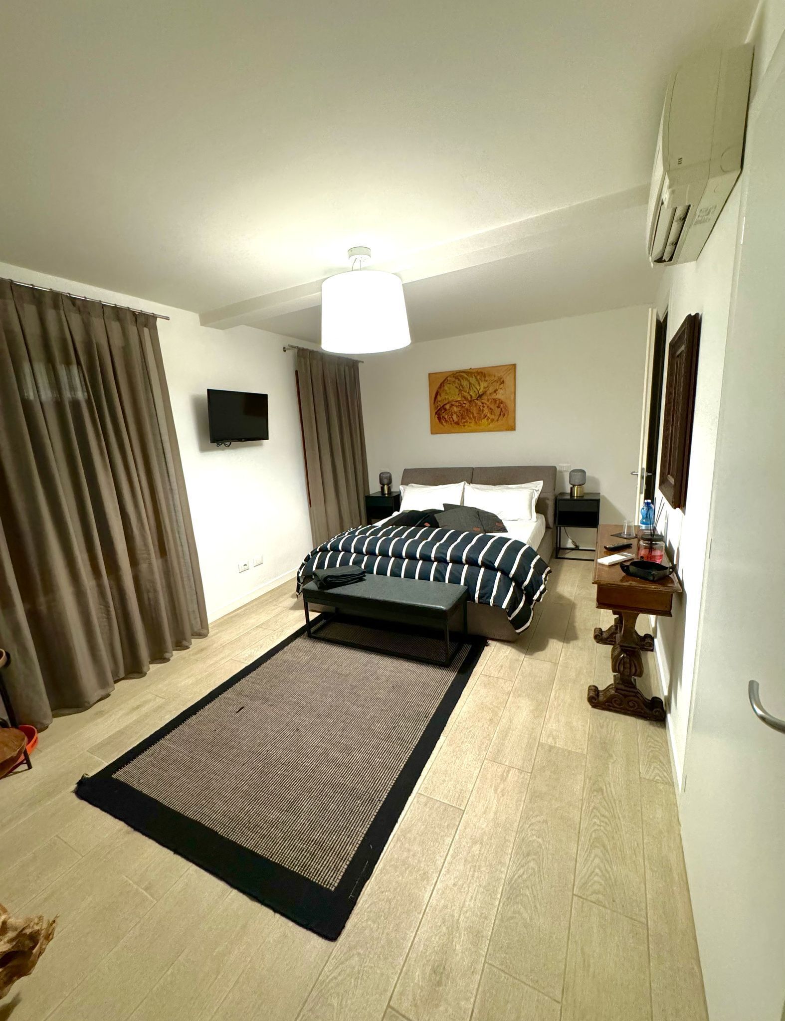 A hotel room with a bed, a desk, a chair, a television, and a painting on the wall.