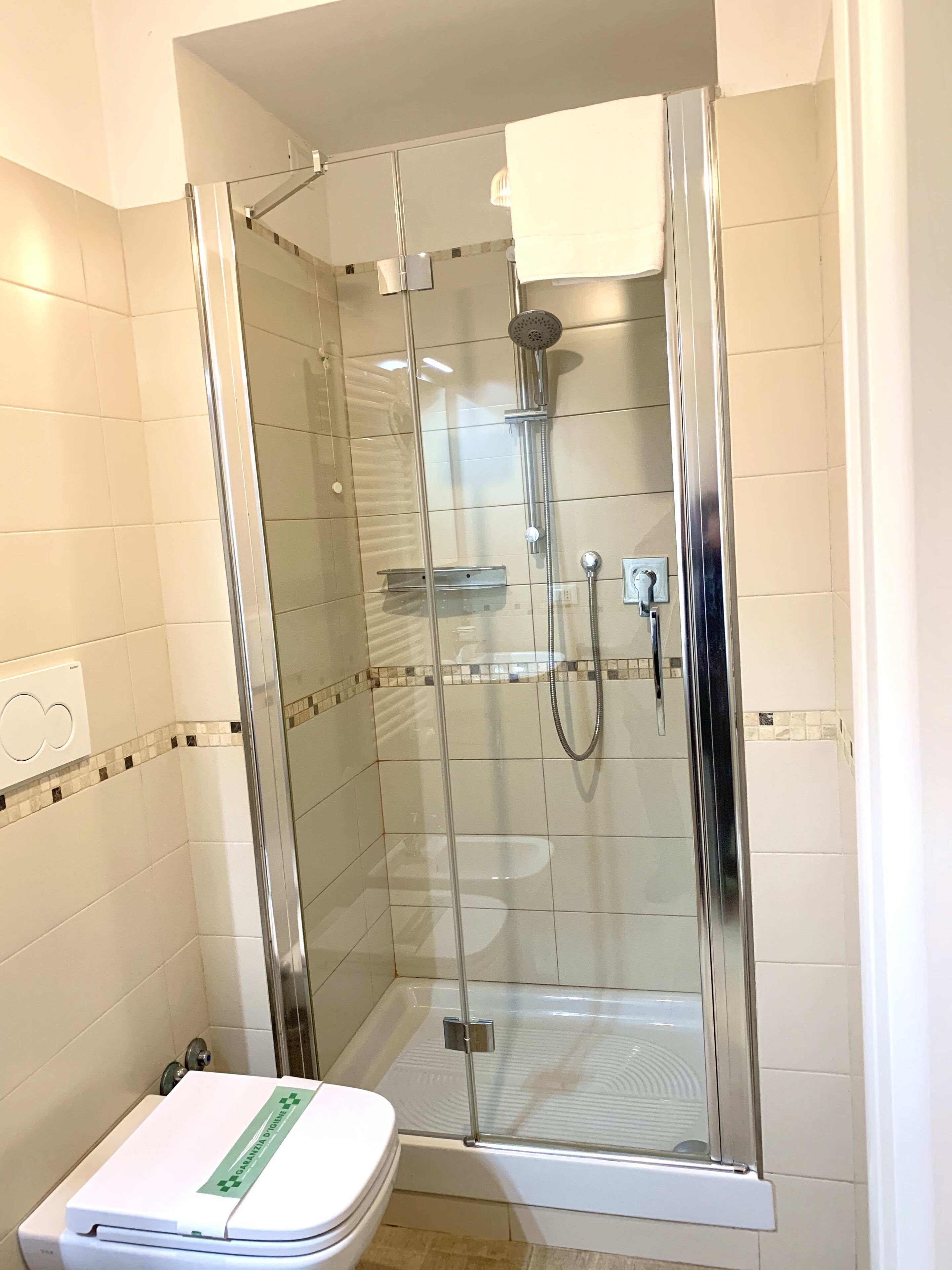 Eine gläserne Duschkabine mit Handbrause und am Wand montiertem Wasserhahn.