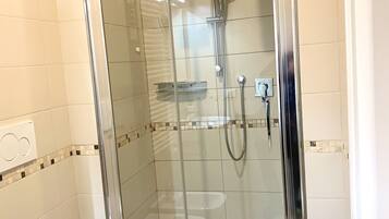 Eine gläserne Duschkabine mit Handbrause und am Wand montiertem Wasserhahn.