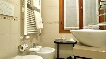 Un baño con inodoro, bidé, lavabo, toallero y ventana con cortinas.