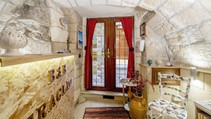 A cozy room with a stone wall, a wooden shelf with letters, a red curtain, a wooden chair, and a vase with flowers. - B&B Eraclio (Barletta)
