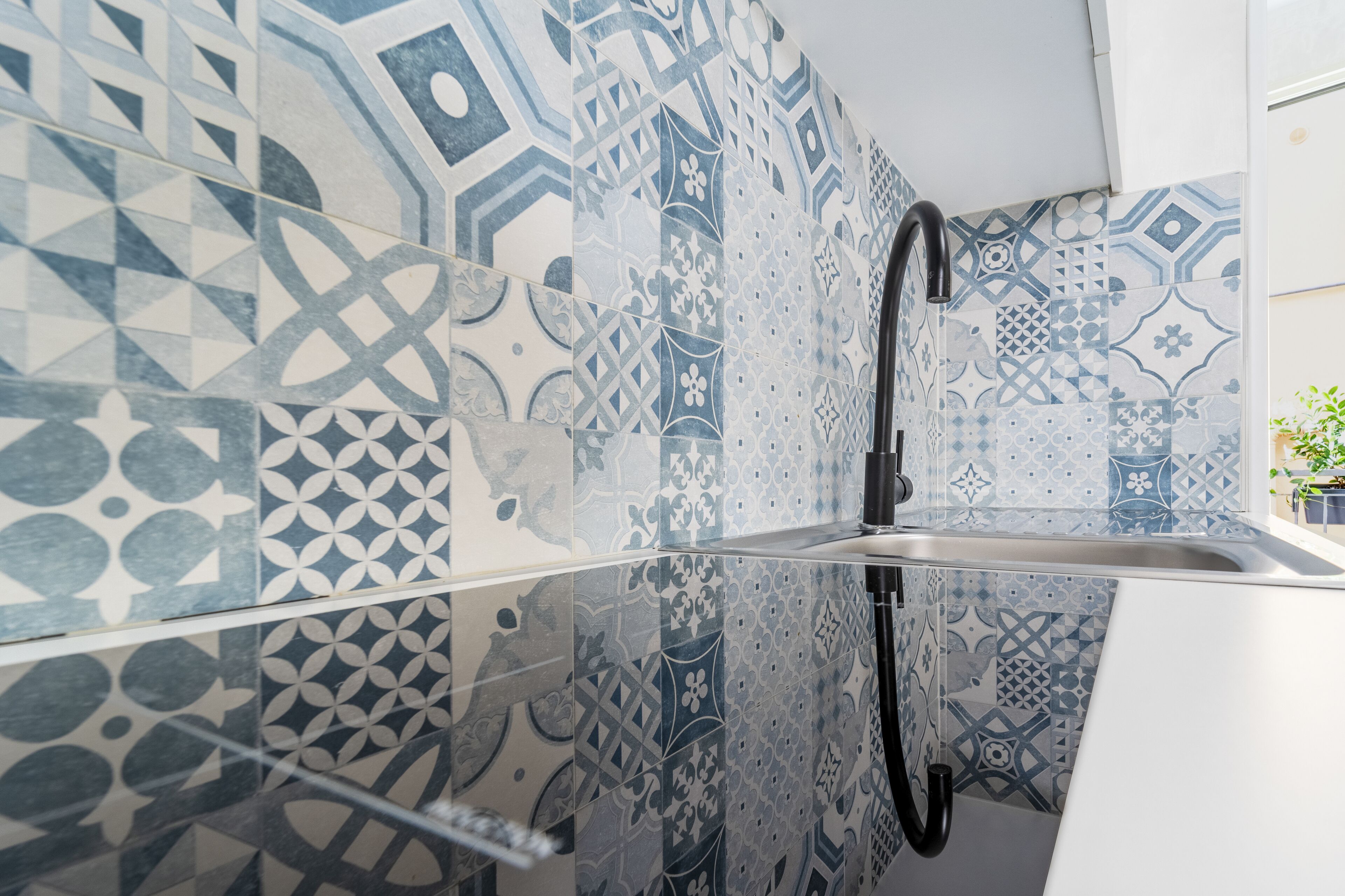 Una cucina moderna con piastrelle decorate, un rubinetto nero e un piano di lavoro bianco.