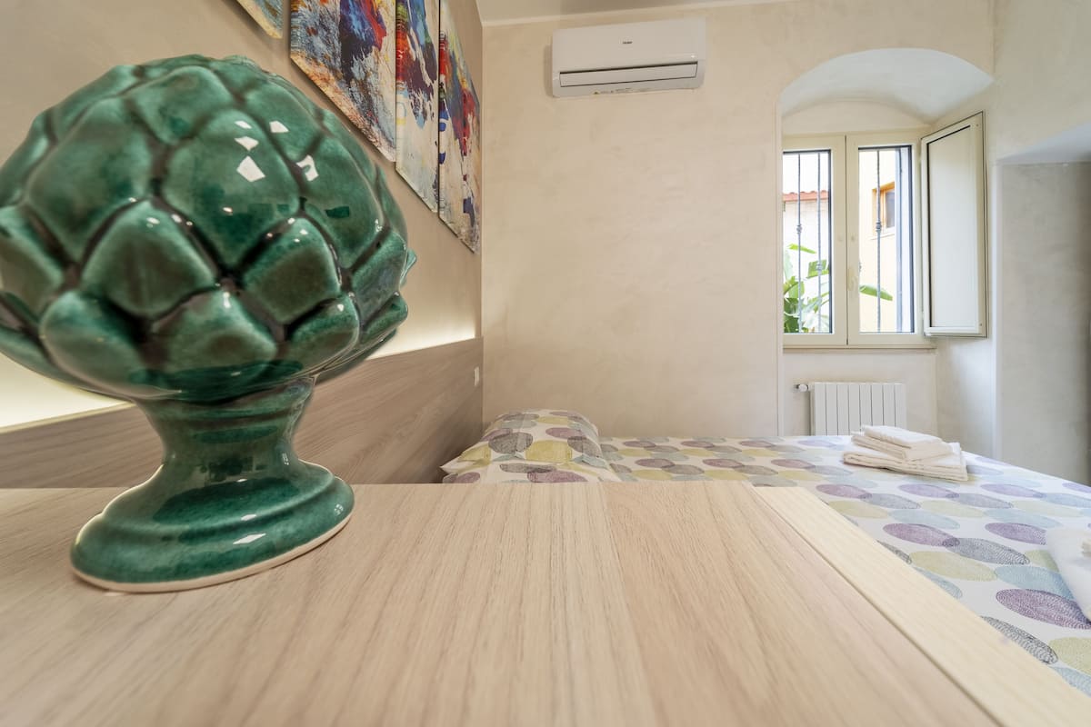 A room with a bed, an air conditioning unit, a window with bars, and a wall-mounted artwork.