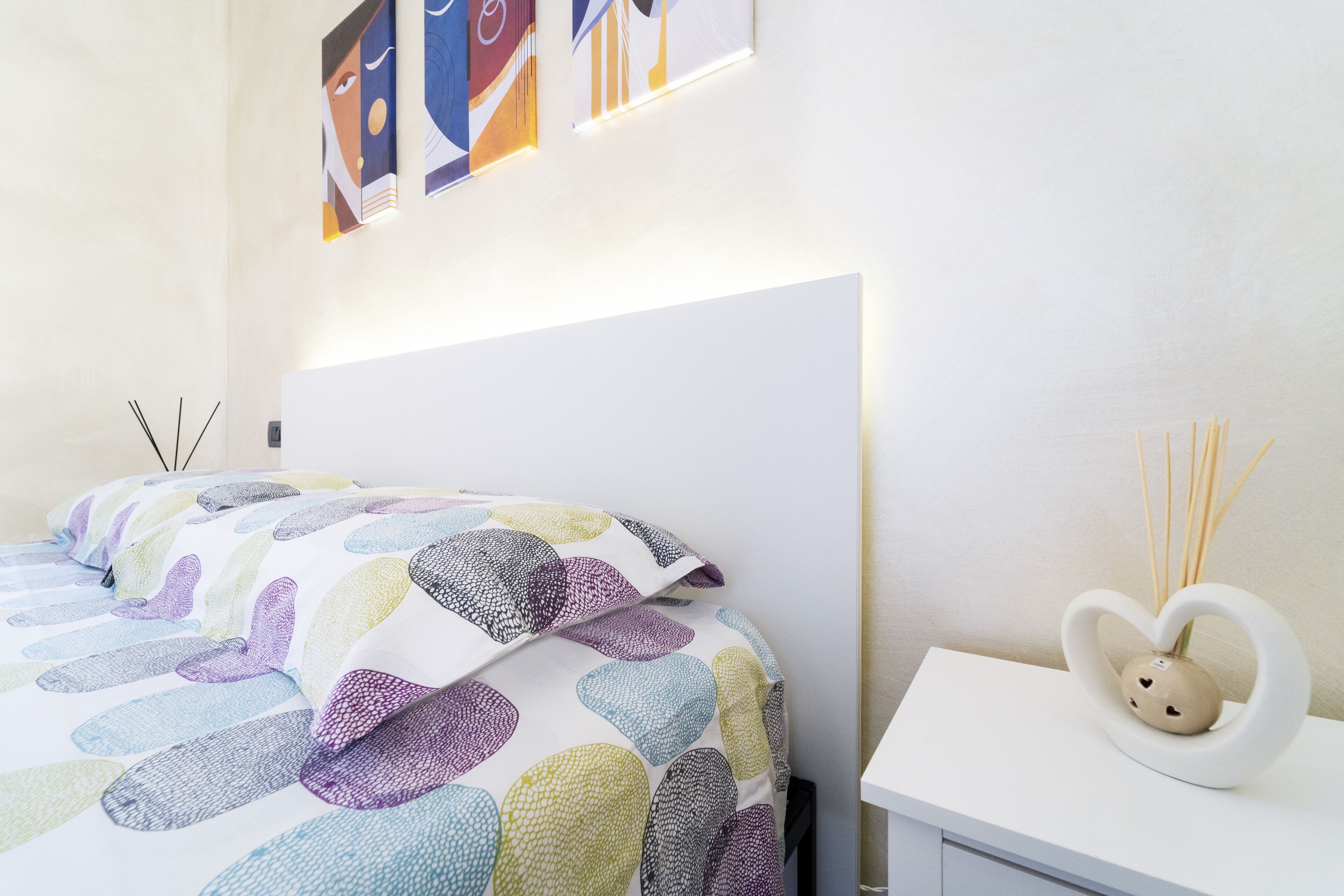 Ein Schlafzimmer mit einem Bett, einem Nachttisch mit einer Vase und abstrakter Kunst an der Wand.