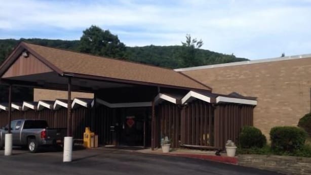 A building with a covered entrance, a parking lot, and a brick wall. - Motel 88 (Oneonta)