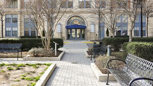 A building entrance with a paved pathway, benches, and a blue awning. - The Gramercy at Metropolitan Park (Arlington)