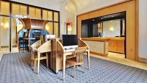A hotel lobby with a reception desk, a computer station, and a seating area with a patterned carpet. - The Gramercy at Metropolitan Park (Arlington)