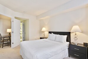 A hotel room with a large bed, two bedside tables with lamps, a desk with a chair, and a closet. - The Gramercy at Metropolitan Park (Arlington)