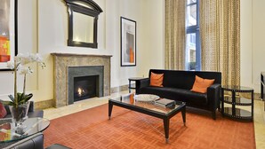 A living room with a fireplace, a black sofa with orange cushions, a glass coffee table, and a patterned curtain. - The Gramercy at Metropolitan Park (Arlington)