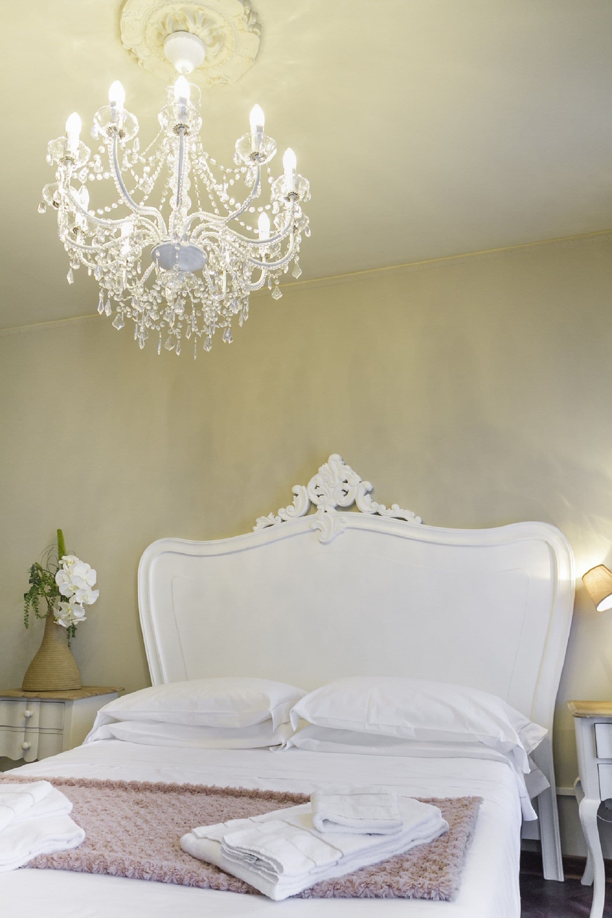 A hotel room with a white bed, a chandelier, and a vase with flowers.