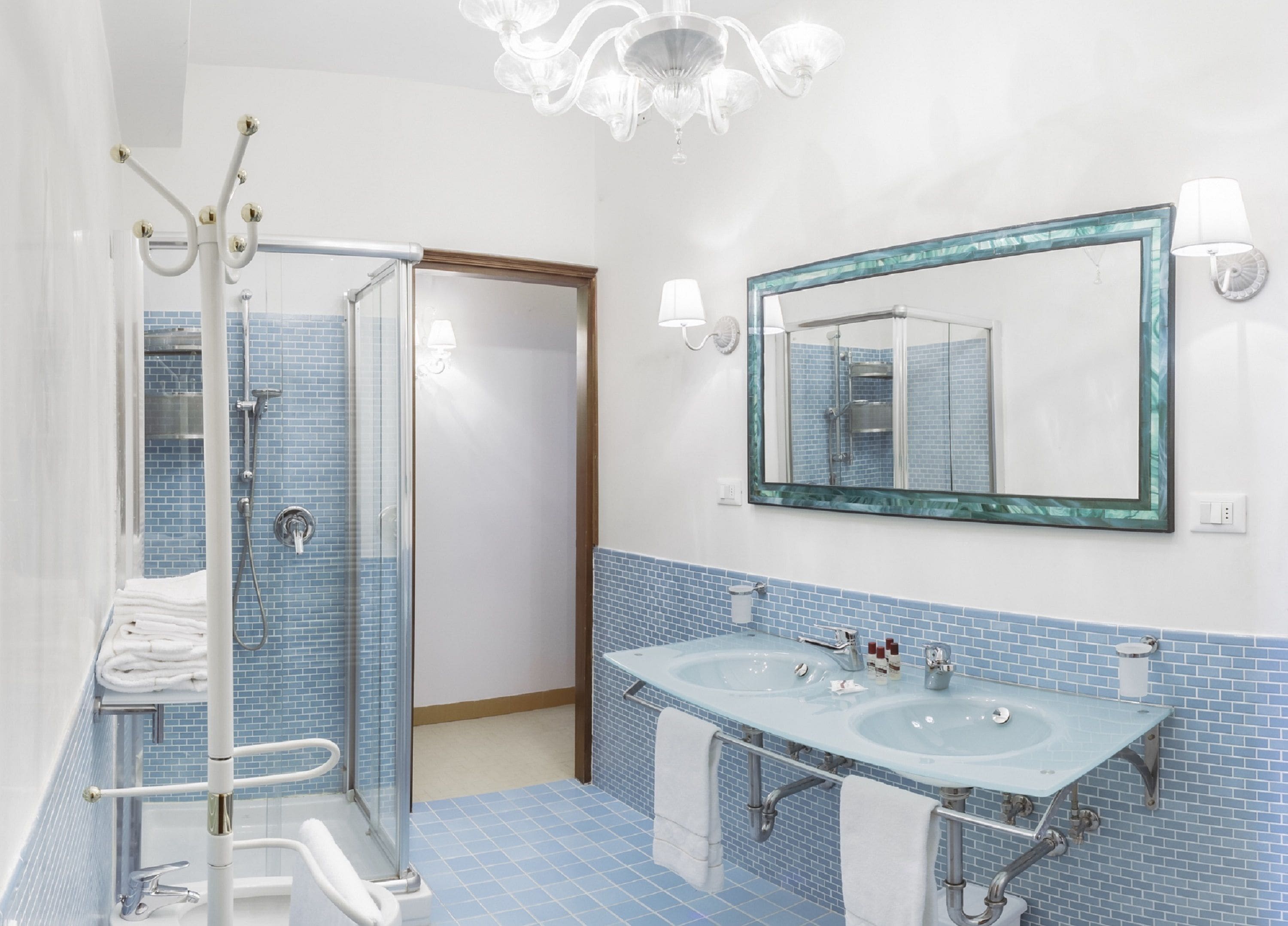 A bathroom with a glass shower enclosure, two sinks, and a large mirror with a decorative frame.