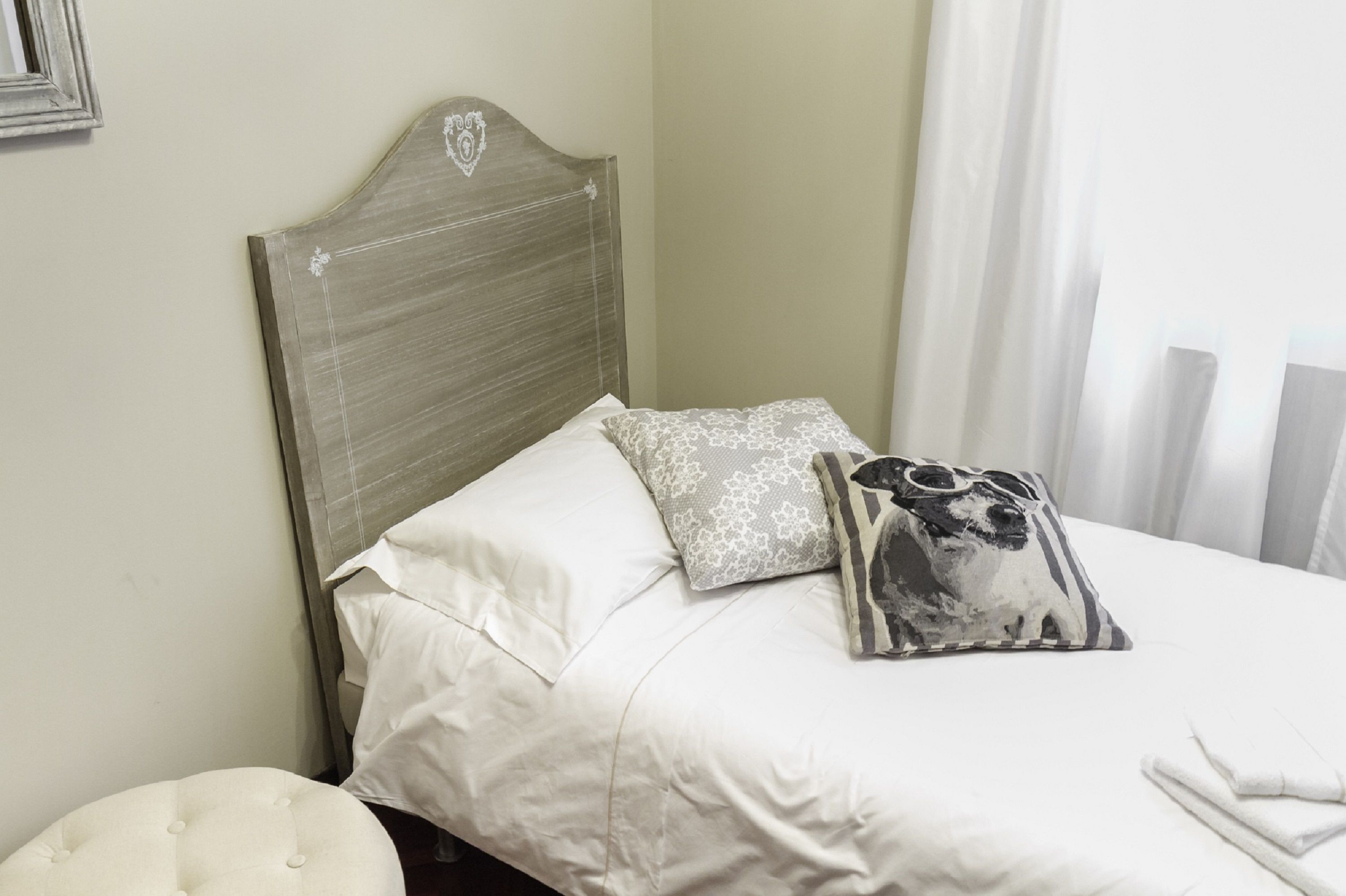 A neatly made bed with white linens and two decorative pillows, one with a floral pattern and another with a black and white design.