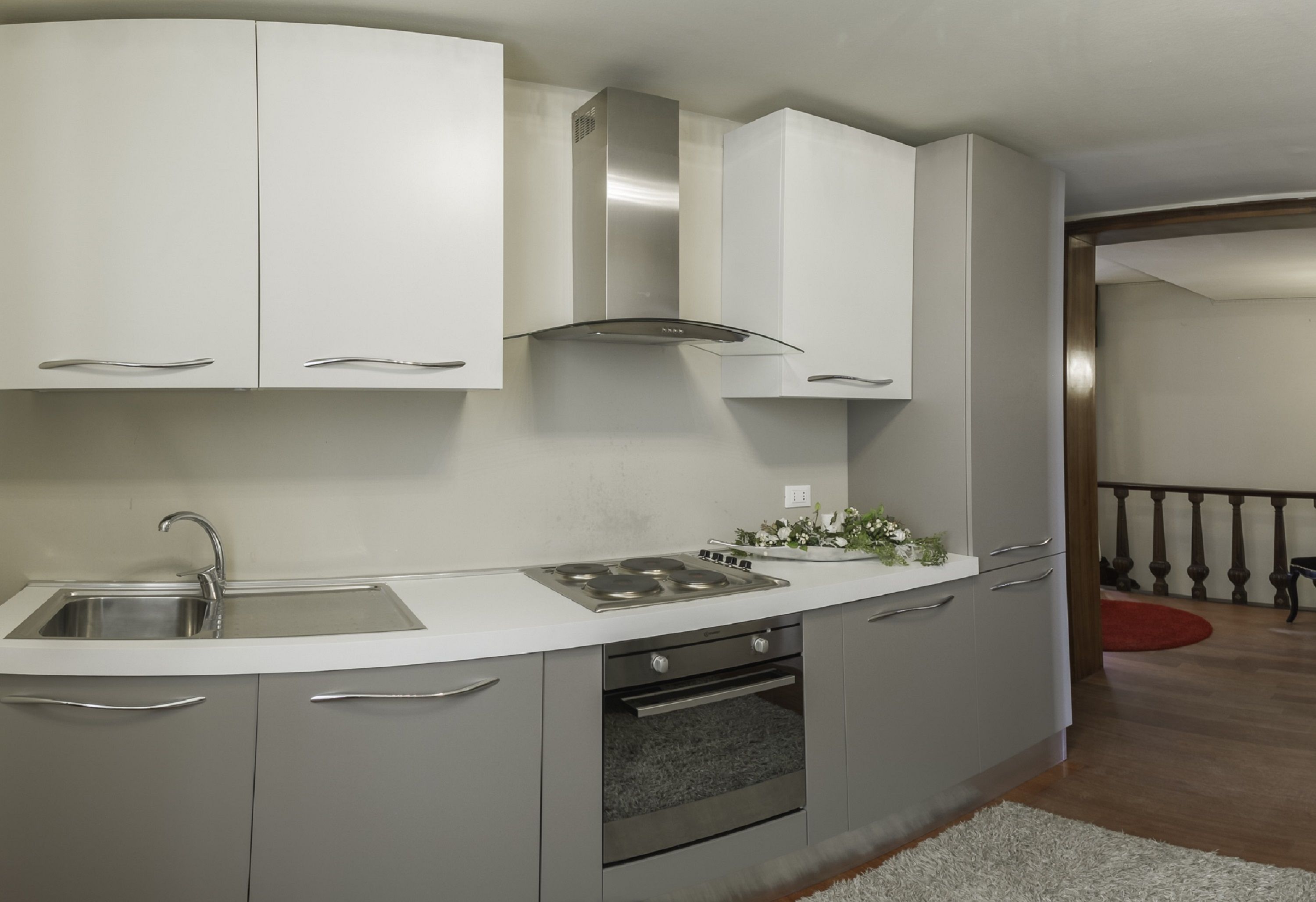 A modern kitchen with a stainless steel sink, a built-in oven, and grey cabinets.