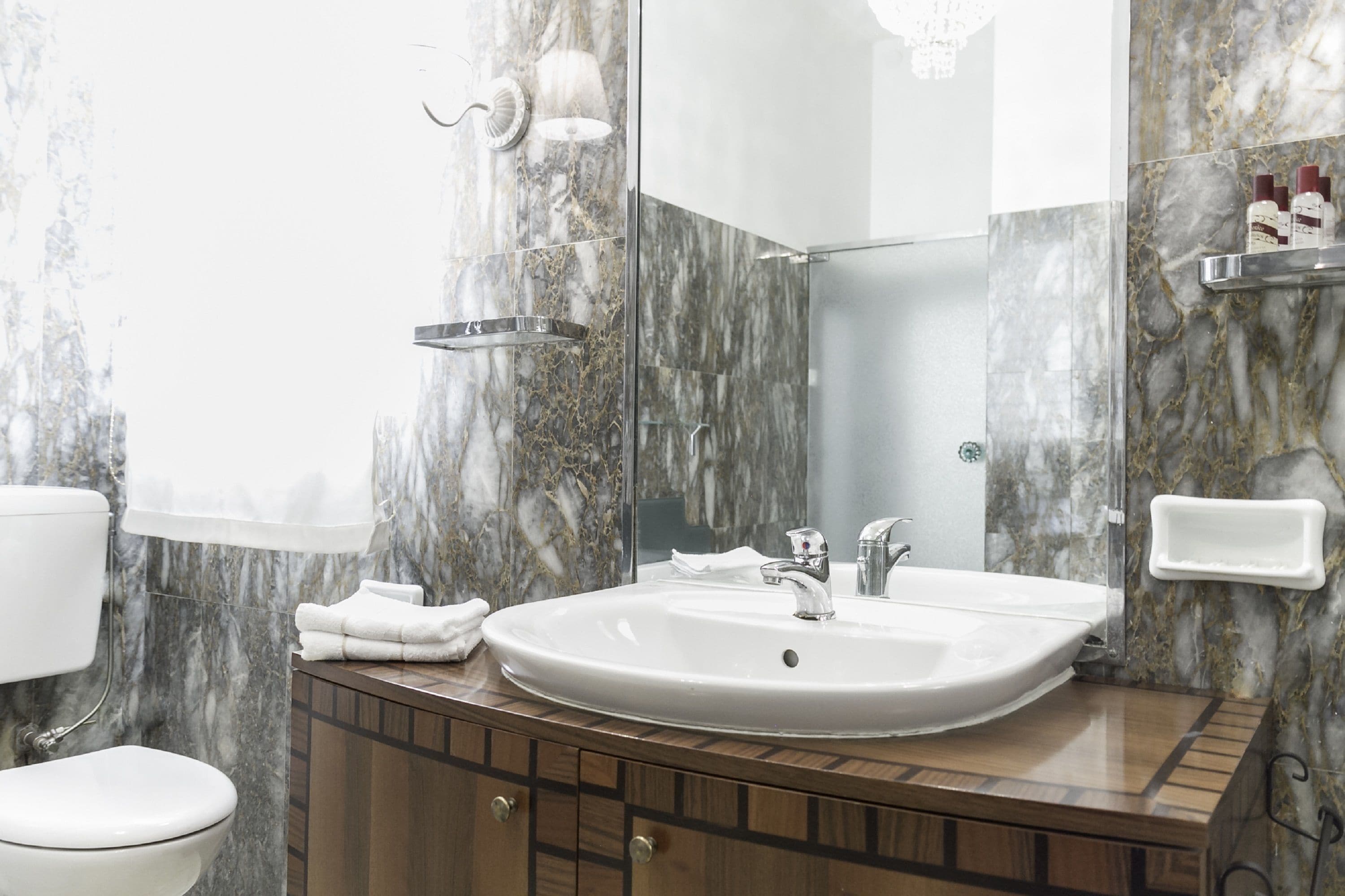 Un baño con pared de mármol, lavamanos blanco y tocador de madera.