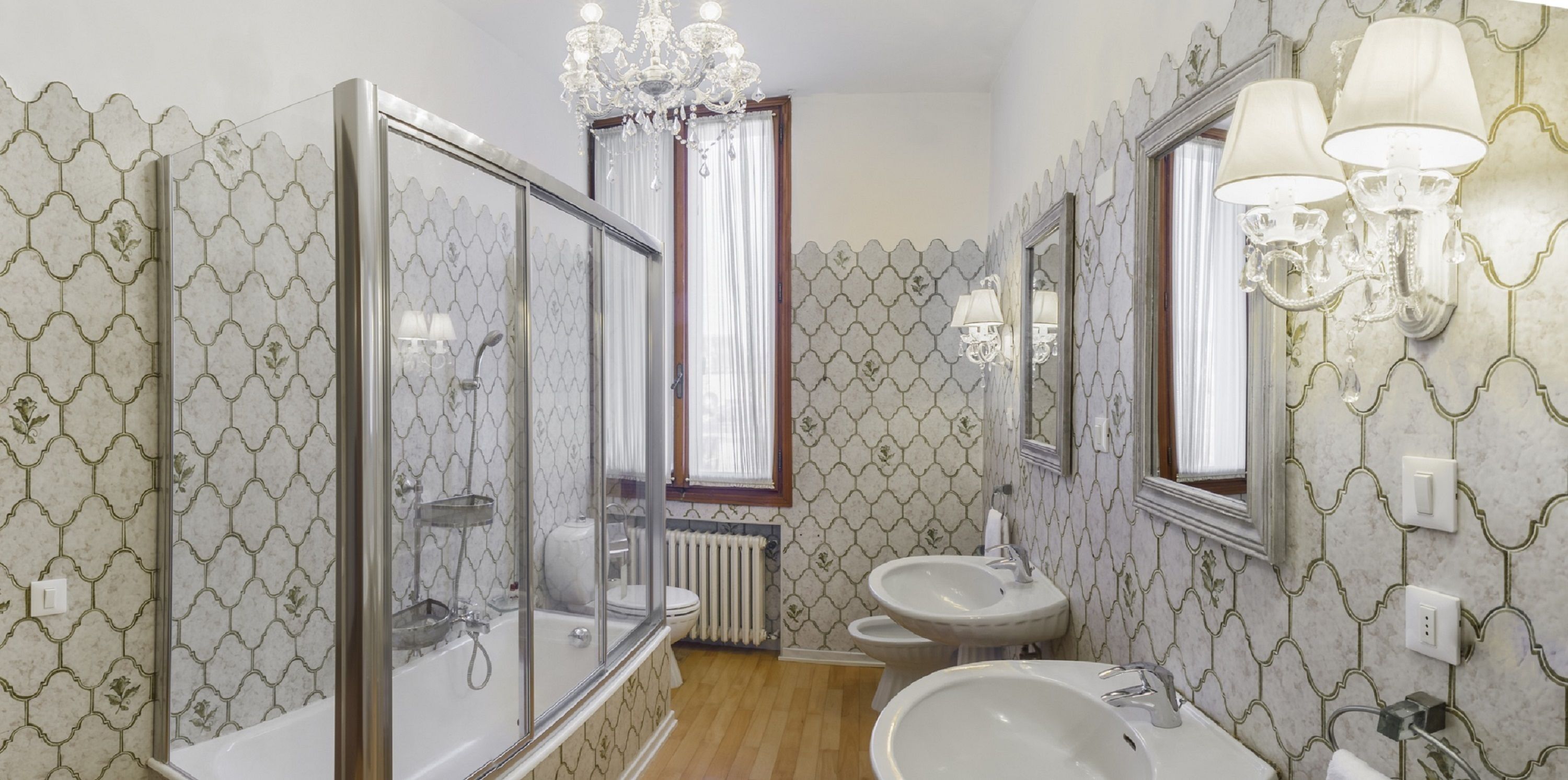 A bathroom with a bathtub, two sinks, a chandelier, and patterned wallpaper.