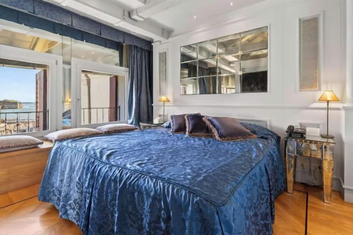 Une chambre avec un grand lit, une table de chevet, un miroir et une vue sur la mer.