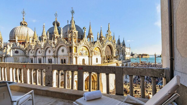A balcony with lounge chairs overlooking a historic building with ornate architecture and a view of the river.