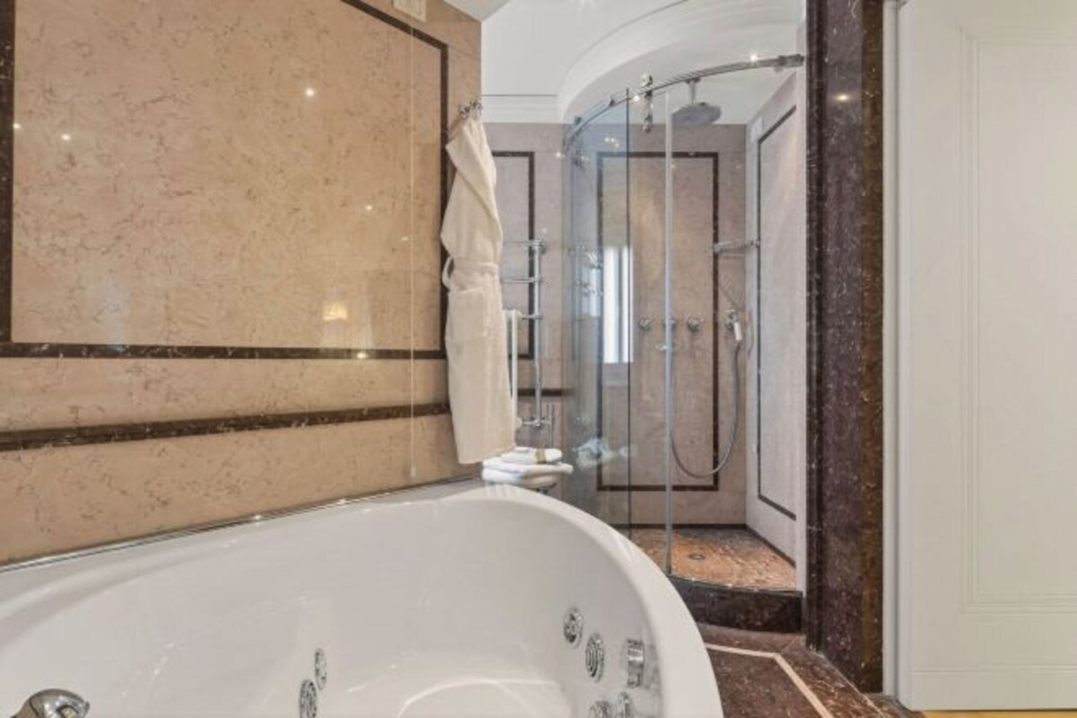Une salle de bain avec une baignoire, une cabine de douche en verre et un revêtement de sol en marbre.