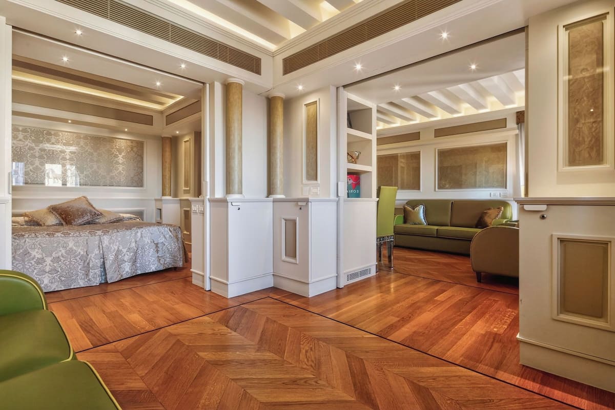 Un vaste espace de vie doté d’un parquet en bois à motifs en chevrons, d’un canapé vert, d’une armoire blanche et d’un fauteuil vert.