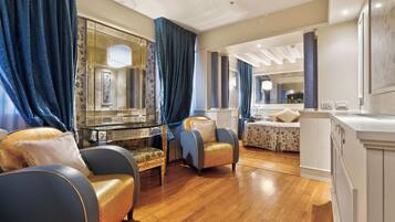 Une chambre spacieuse avec un grand lit, un coin salon comprenant un fauteuil et une petite table, ainsi qu’un grand miroir.