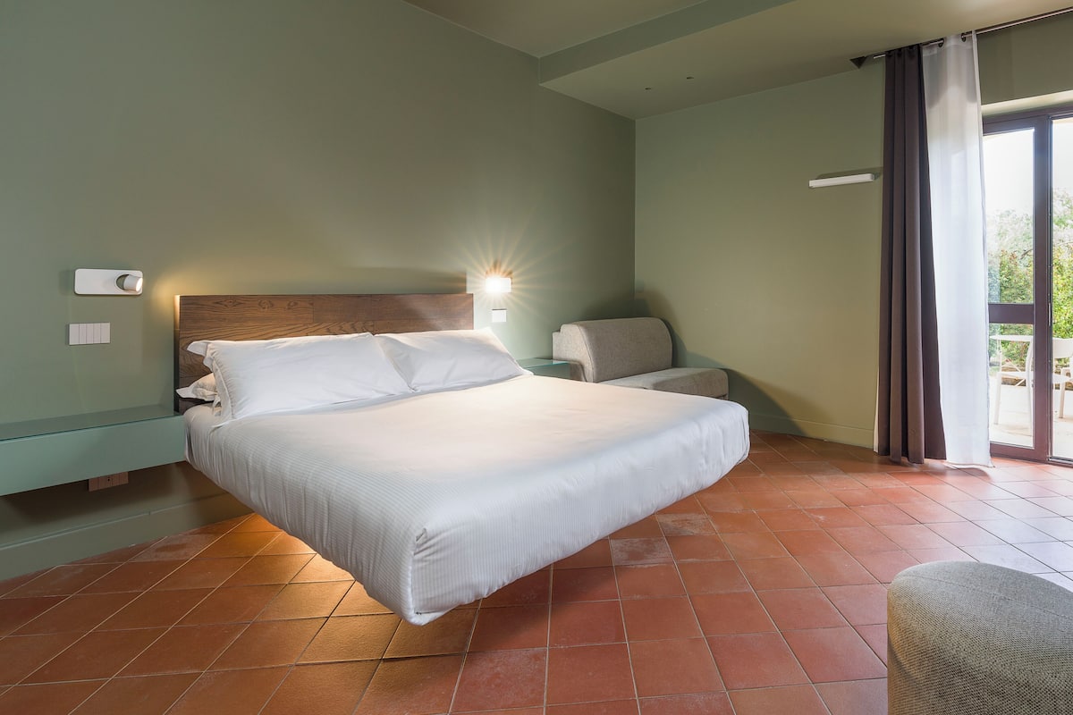 Una habitación de hotel con una cama, una silla, una mesita de noche y un ventanal con cortinas.