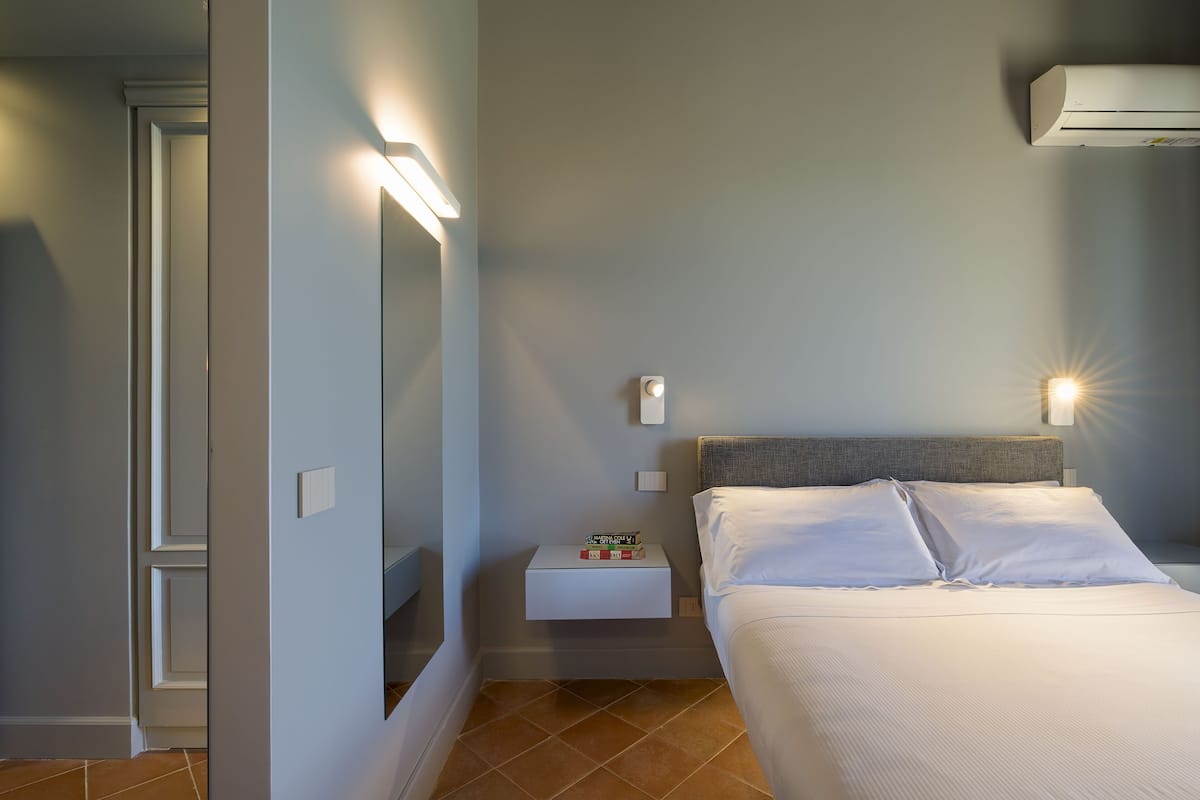 Una habitación de hotel con cama, mesita de noche y aire acondicionado de pared.