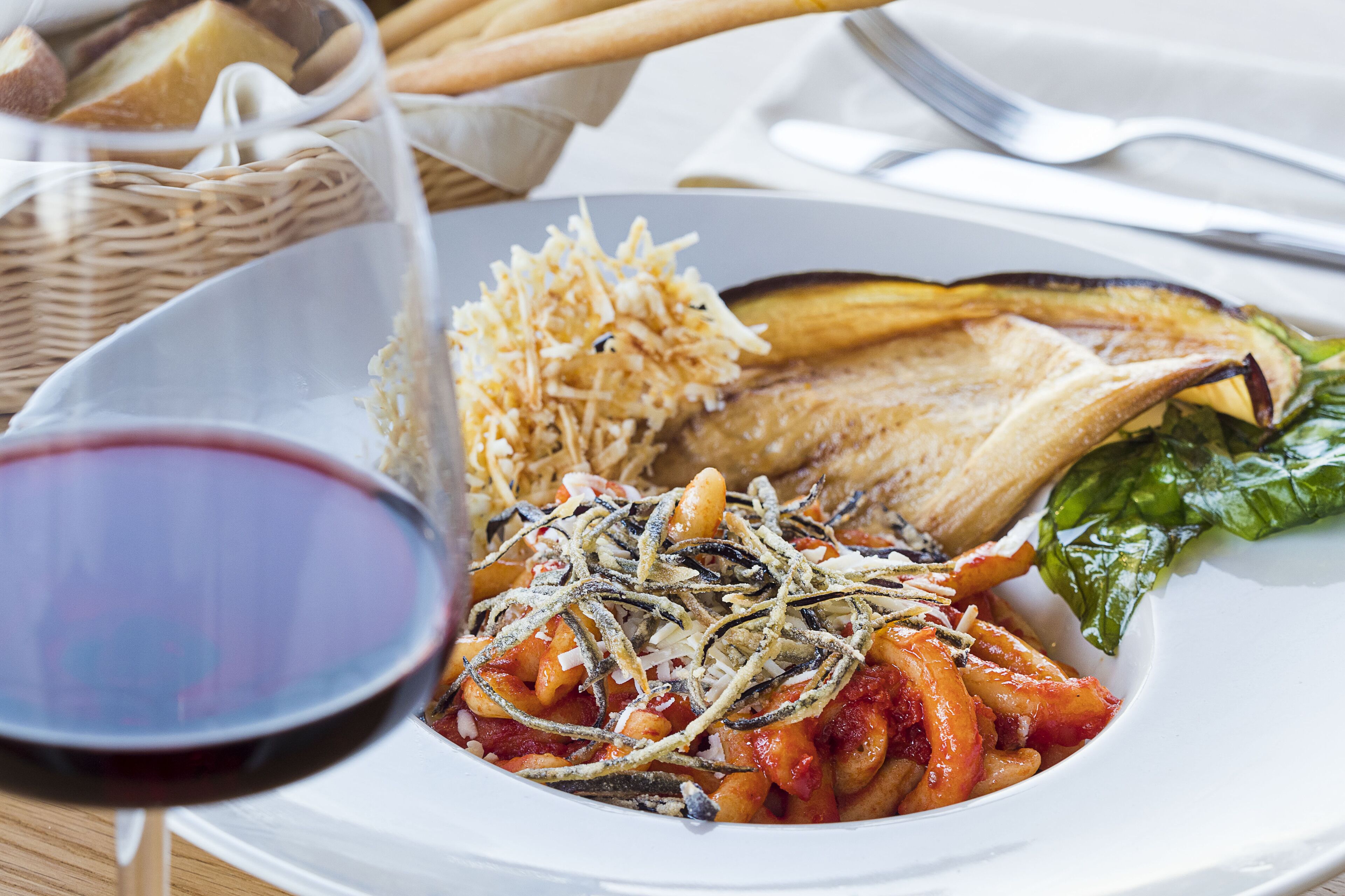 Un plato de comida con pasta, una rebanada de pan y una copa de vino tinto.