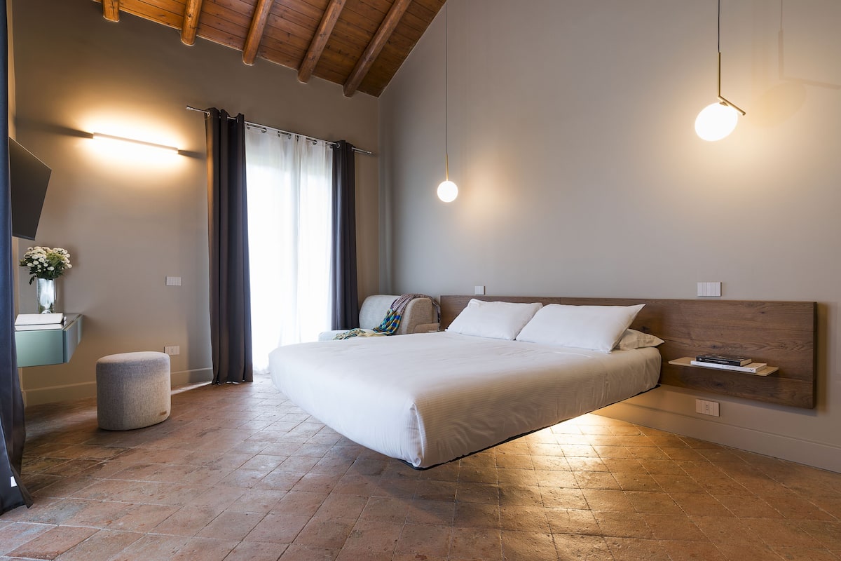 Un dormitorio con una cama grande, una mesita de noche, una lámpara colgante y un cabecero de madera.