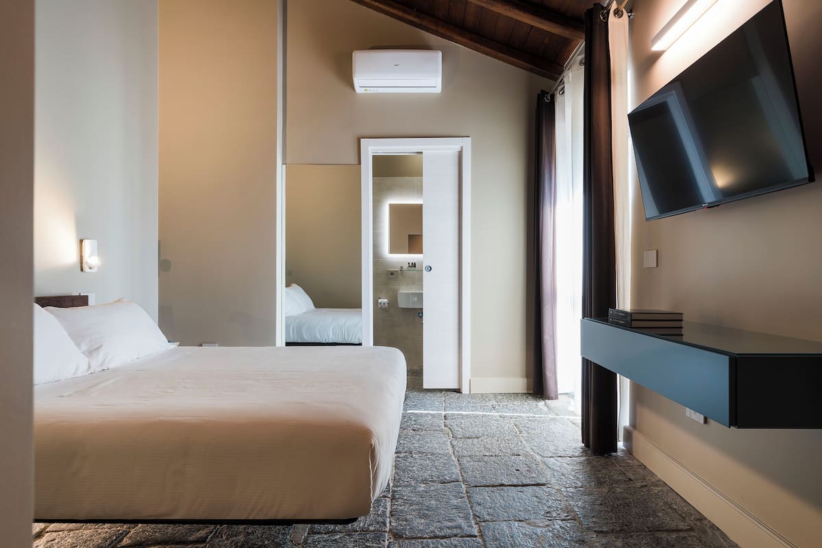 Una habitación de hotel con cama, televisión montada en la pared y suelo de piedra.